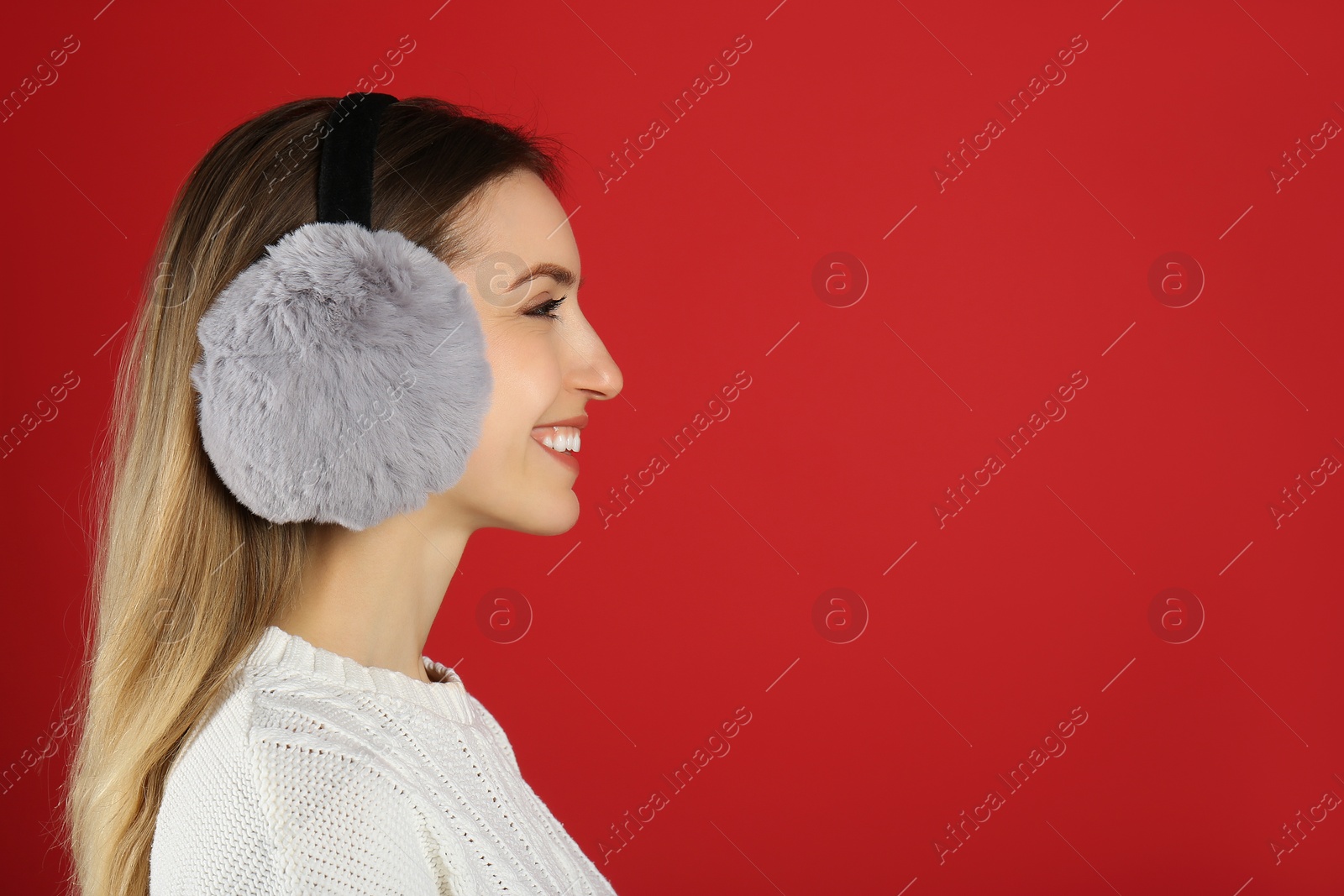 Photo of Happy woman wearing warm earmuffs on red background, space for text