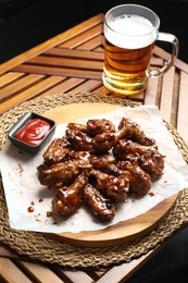 Photo of Tasty chicken wings, mug of beer and ketchup on wooden table. Delicious snack