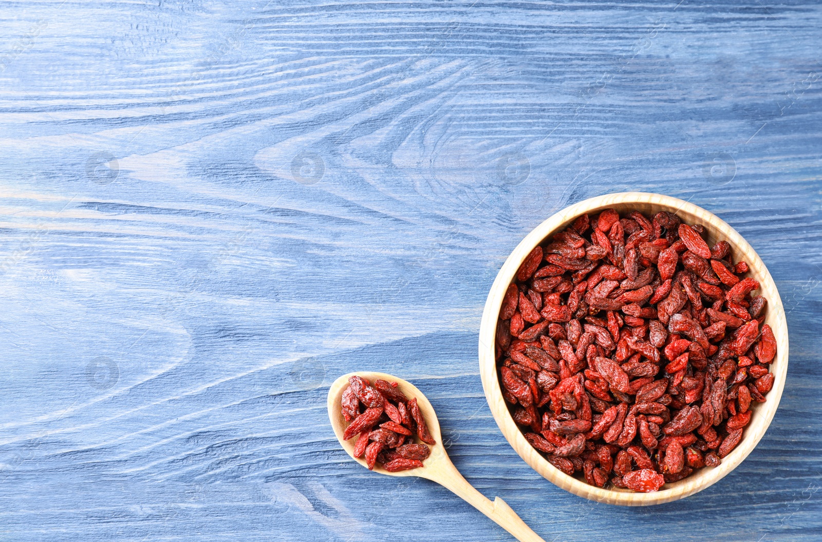 Photo of Dry goji berries on blue wooden table, flat lay. Space for text