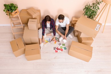 Photo of Happy couple surrounded by moving boxes choosing colors in new apartment, above view