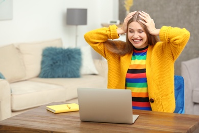 Happy young woman playing online lottery using laptop at home