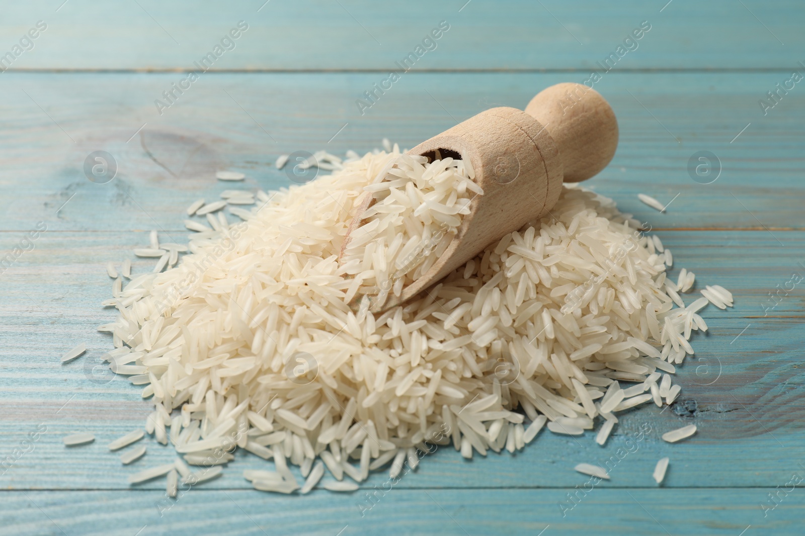 Photo of Raw basmati rice and scoop on light blue wooden table