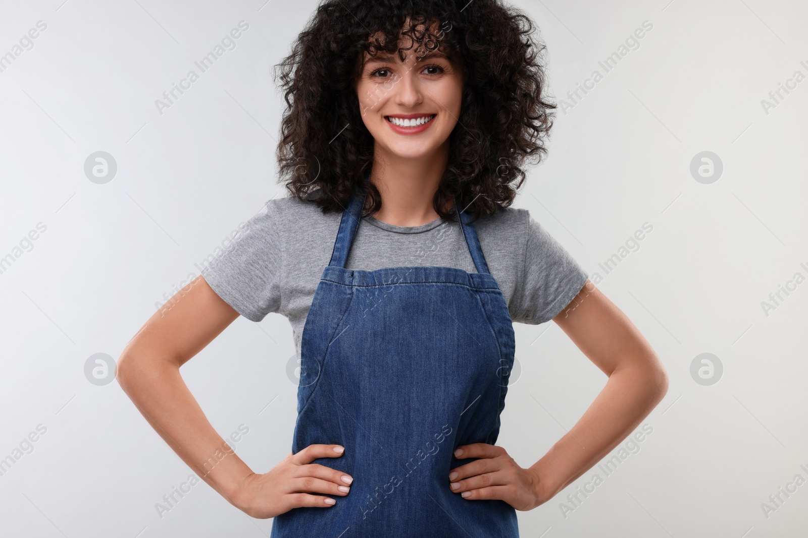 Photo of Happy woman wearing kitchen apron on light grey background. Mockup for design