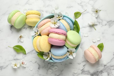 Photo of Delicious colorful macarons and flowers on white marble table, flat lay