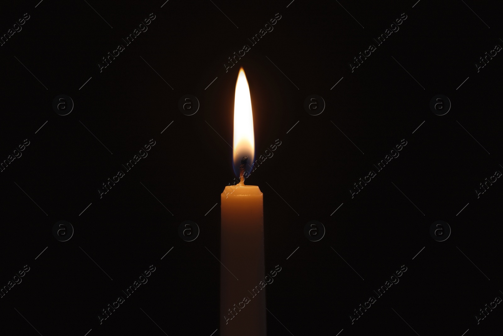 Photo of Wax candle burning on black background, closeup