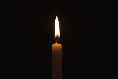 Photo of Wax candle burning on black background, closeup