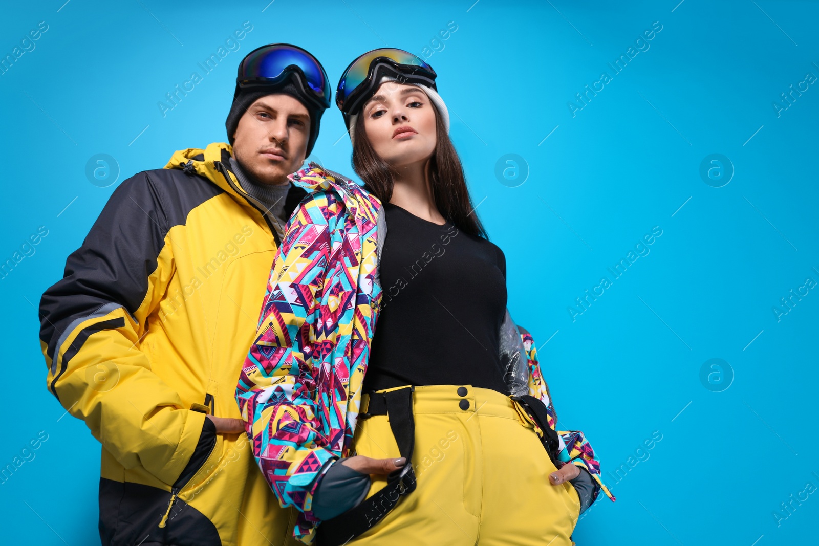 Photo of Couple wearing stylish winter sport clothes on light blue background, low angle view