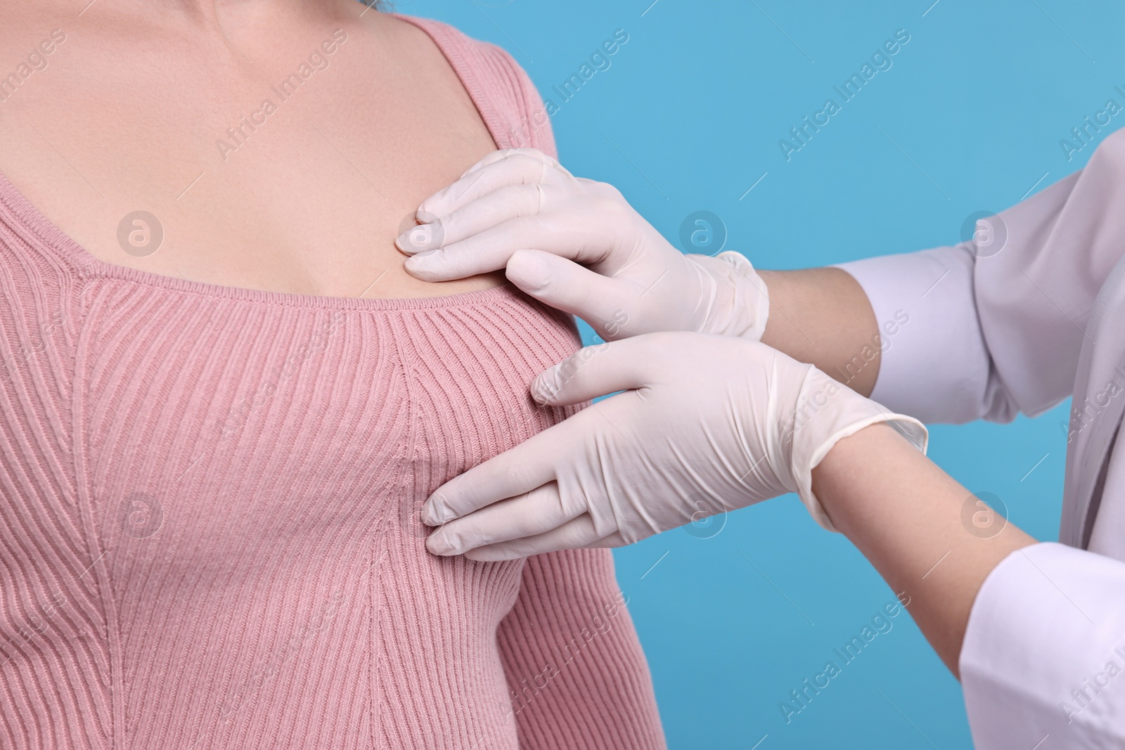 Photo of Mammologist checking woman's breast on light blue background, closeup