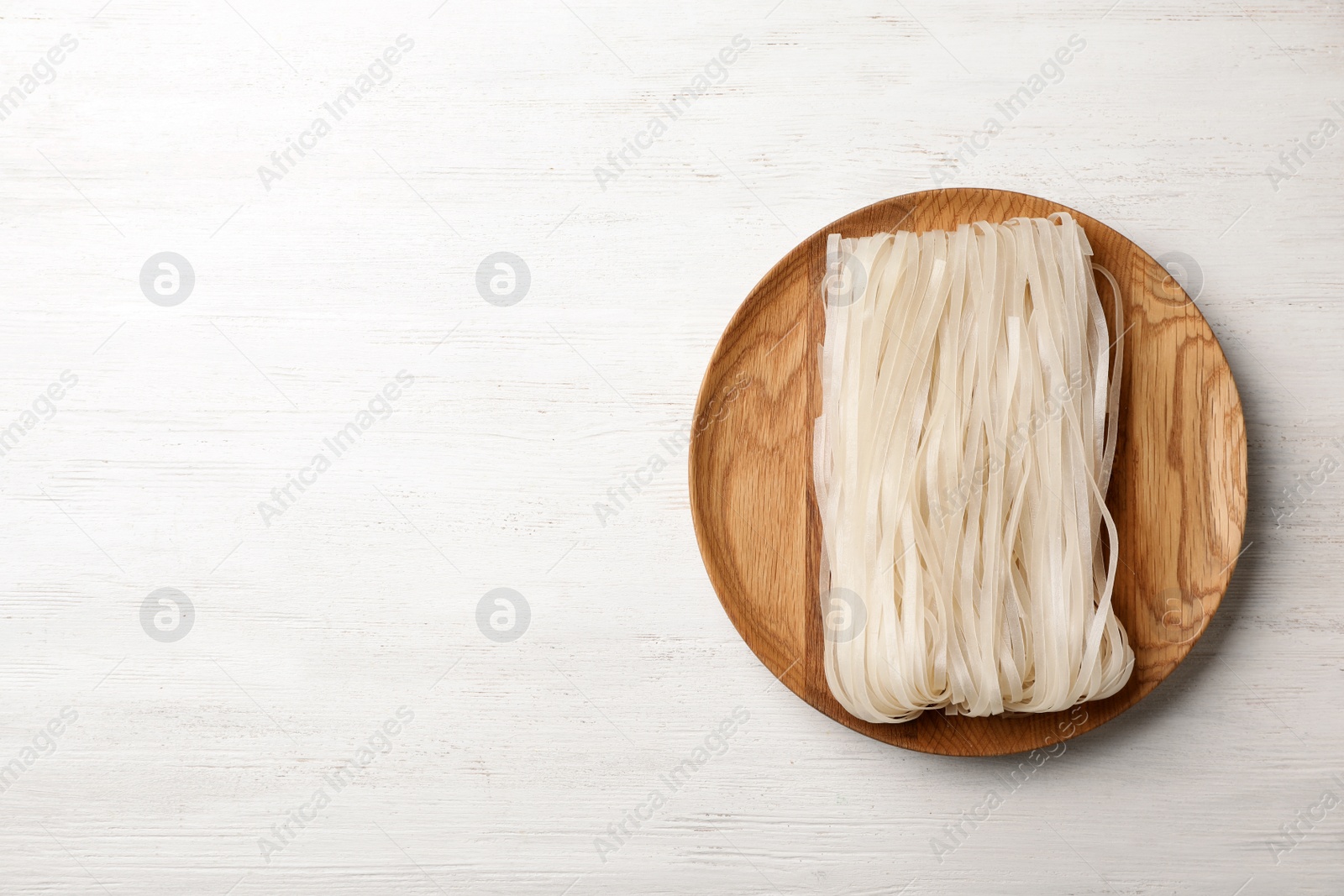 Photo of Plate with raw rice noodles on wooden background, top view. Space for text