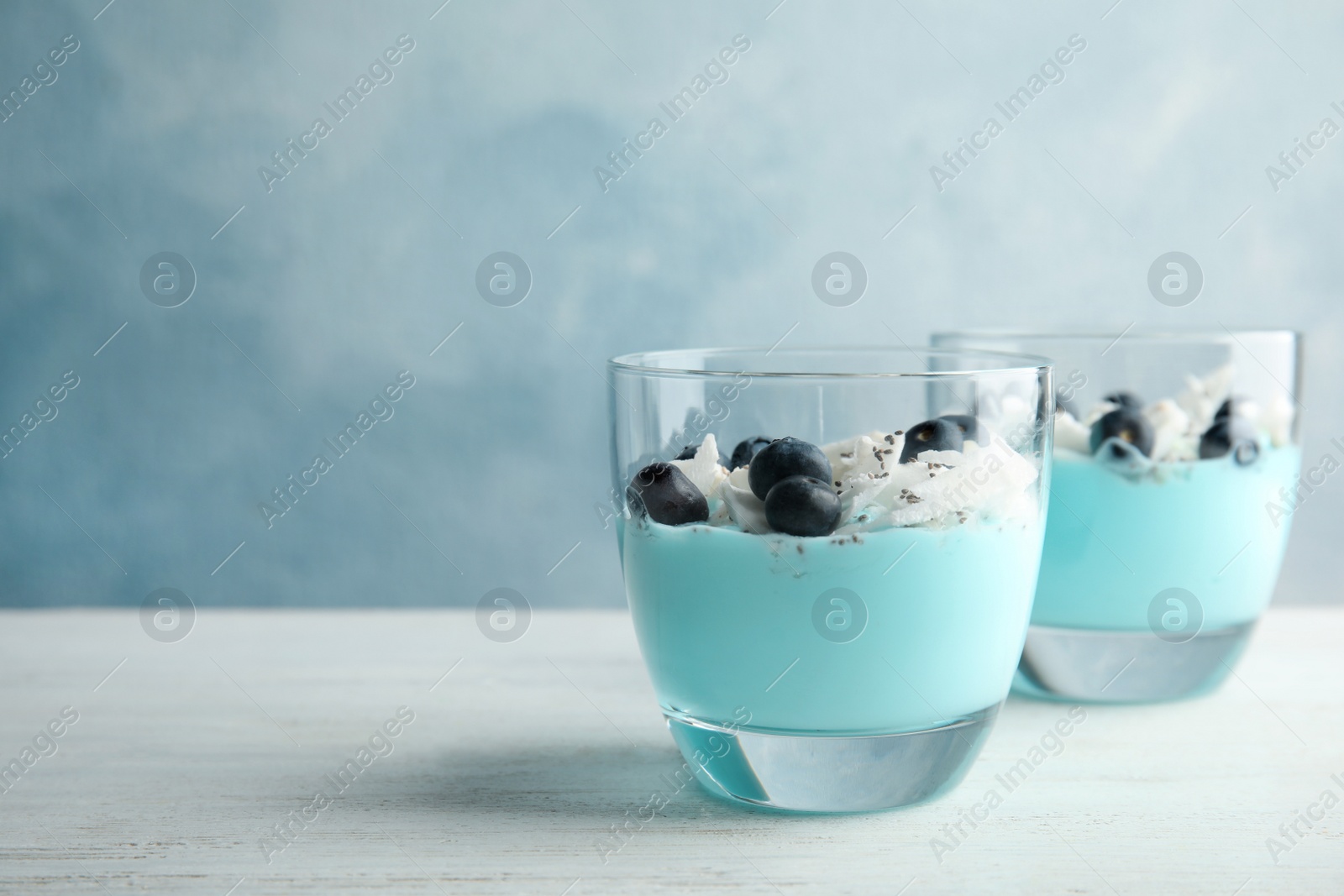 Photo of Glass cups of spirulina smoothie on table against color background. Space for text