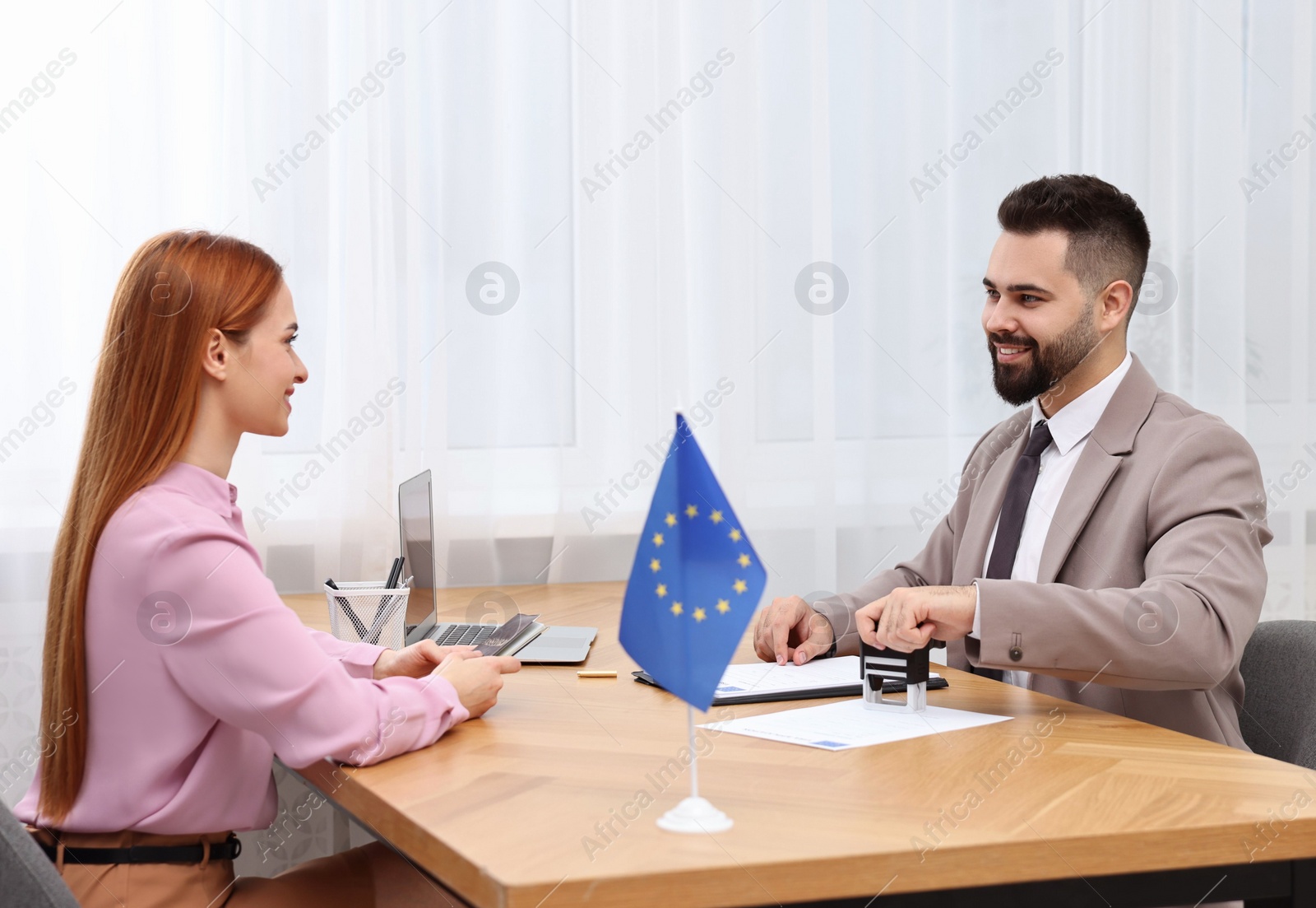 Photo of Immigration to European Union. Embassy worker approving visa application form to woman in office