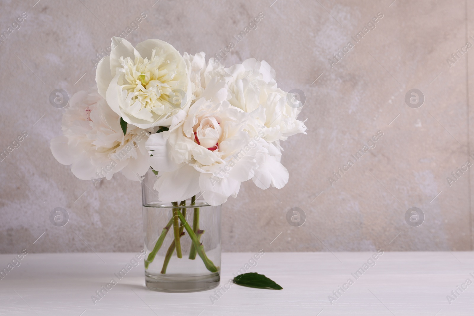 Photo of Beautiful peonies in glass vase on white table. Space for text