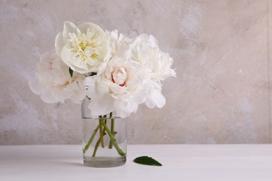 Beautiful peonies in glass vase on white table. Space for text