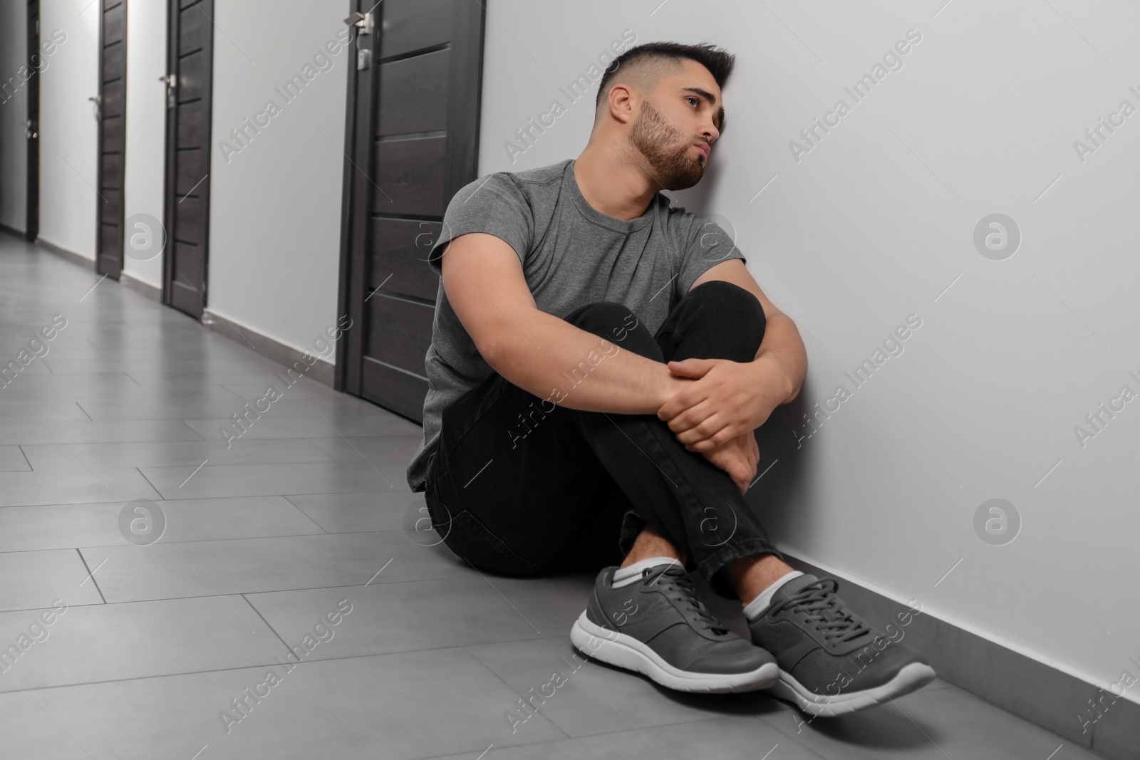 Photo of Sad man sitting on floor in hall. Space for text