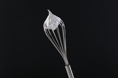 Photo of Whisk with whipped cream on black background