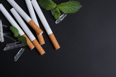 Photo of Cigarettes, menthol crystals and mint on black background, flat lay. Space for text