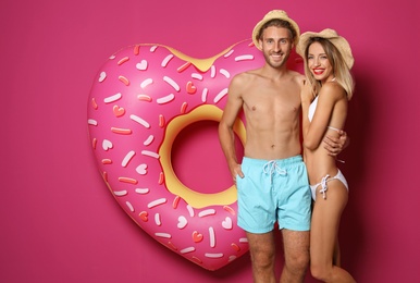 Photo of Happy young couple in beachwear with inflatable ring on color background