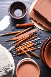 Photo of Clay, dishes and set of crafting tools on black table, flat lay