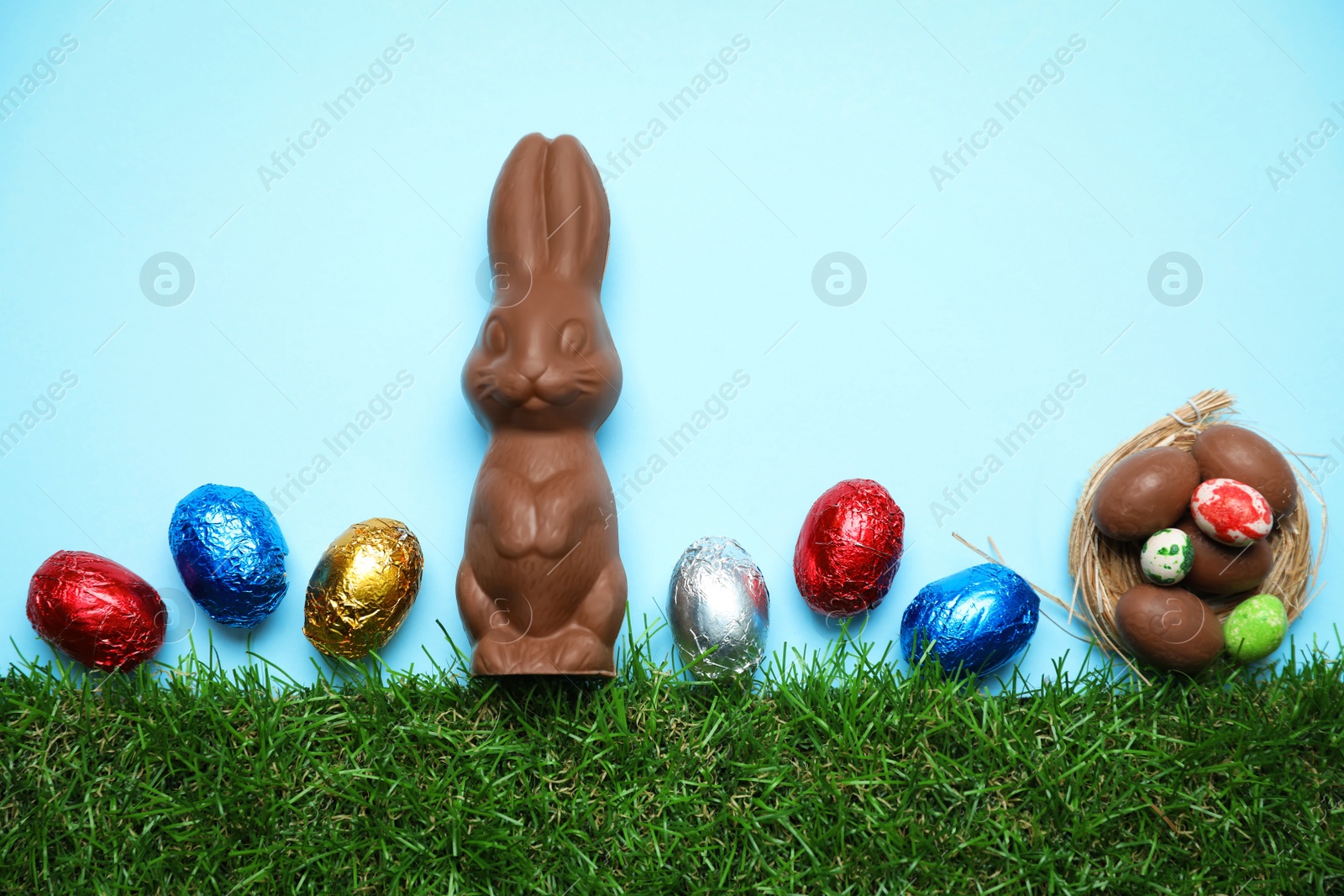 Photo of Chocolate Easter bunny and eggs with green grass on light blue background