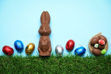 Photo of Chocolate Easter bunny and eggs with green grass on light blue background