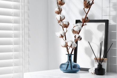 Photo of Reed diffuser, candle and cotton branches with fluffy flowers on white wooden table indoors. Space for text
