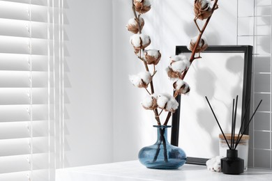 Reed diffuser, candle and cotton branches with fluffy flowers on white wooden table indoors. Space for text