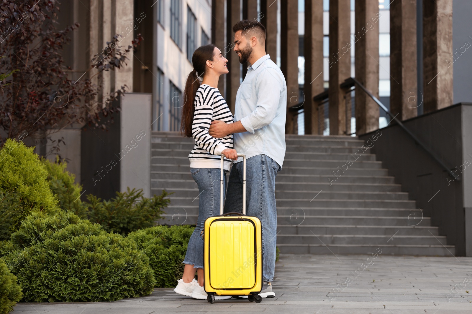 Photo of Long-distance relationship. Beautiful young couple with suitcase near building outdoors