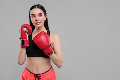 Portrait of beautiful woman in boxing gloves on grey background. Space for text