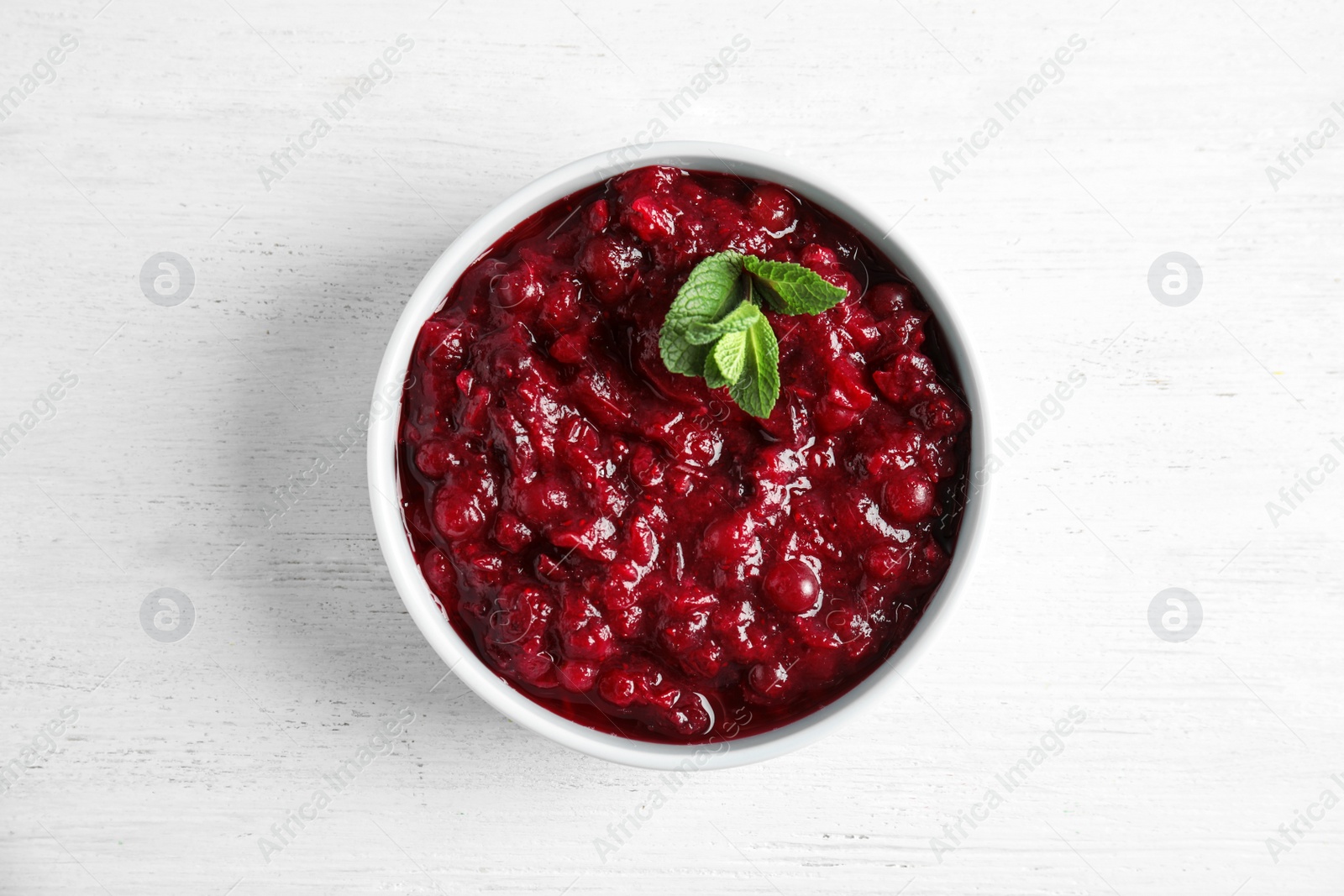 Photo of Bowl of tasty cranberry sauce with sauce on white wooden background, top view