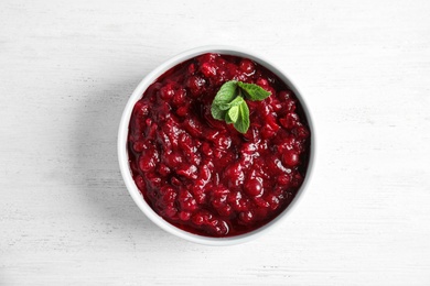 Photo of Bowl of tasty cranberry sauce with sauce on white wooden background, top view