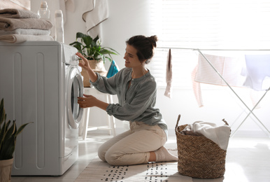 Photo of Young woman using washing machine at home
