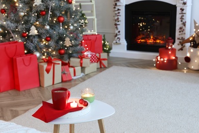 Candles and red cup on white table in room with Christmas decorations. Festive interior design