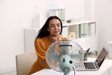 Photo of Young woman enjoying air flow from fan at workplace