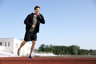 Photo of Young sportsman with wireless earphones running at stadium
