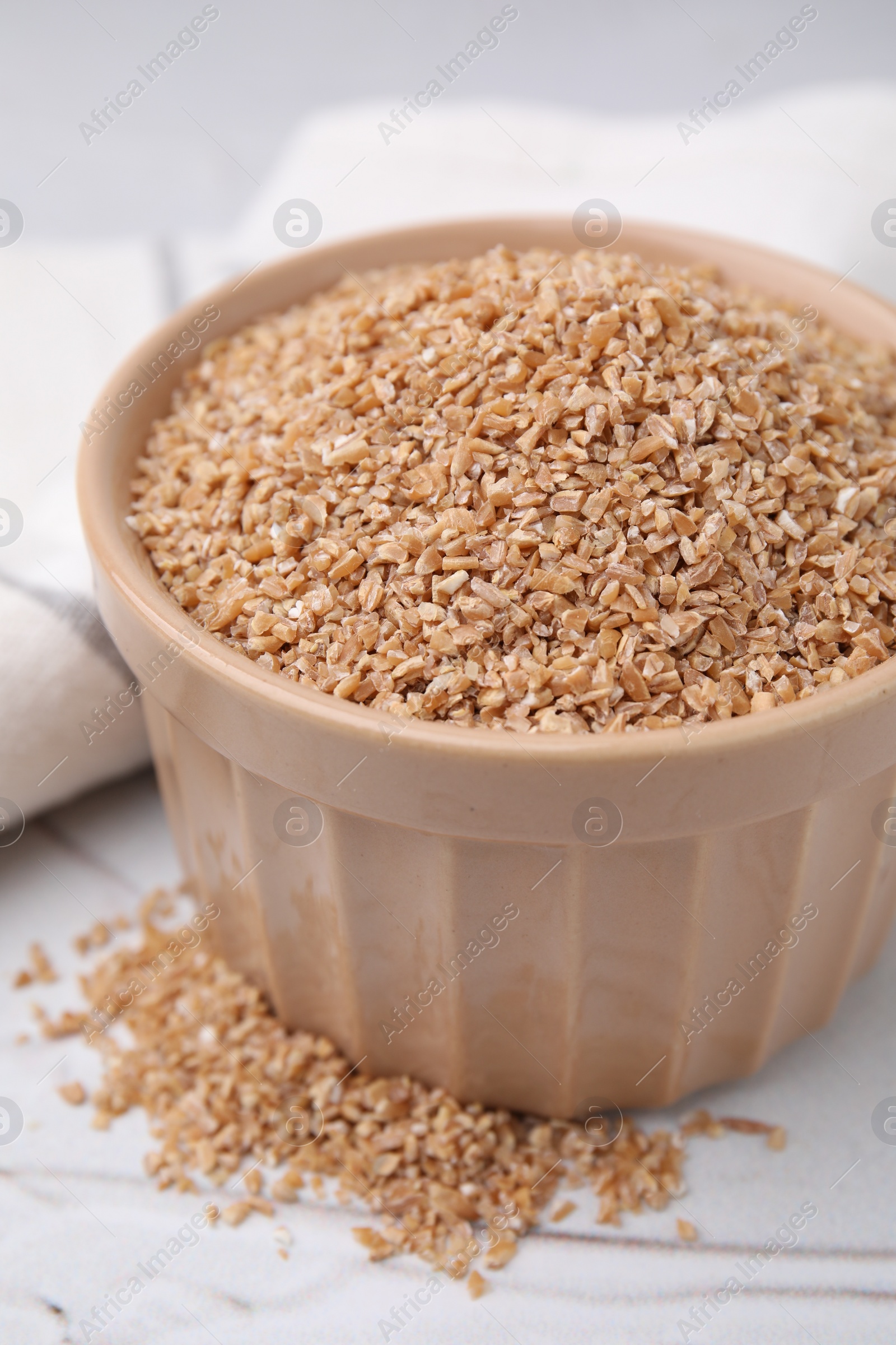 Photo of Dry wheat groats in bowl on white textured table, closeup