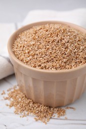 Dry wheat groats in bowl on white textured table, closeup