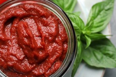 Jar of tasty tomato paste and basil on table, top view
