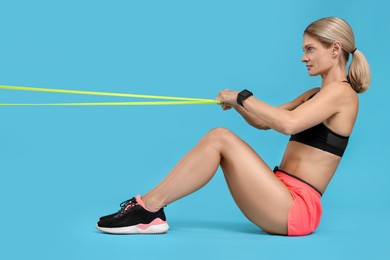 Woman exercising with elastic resistance band on light blue background