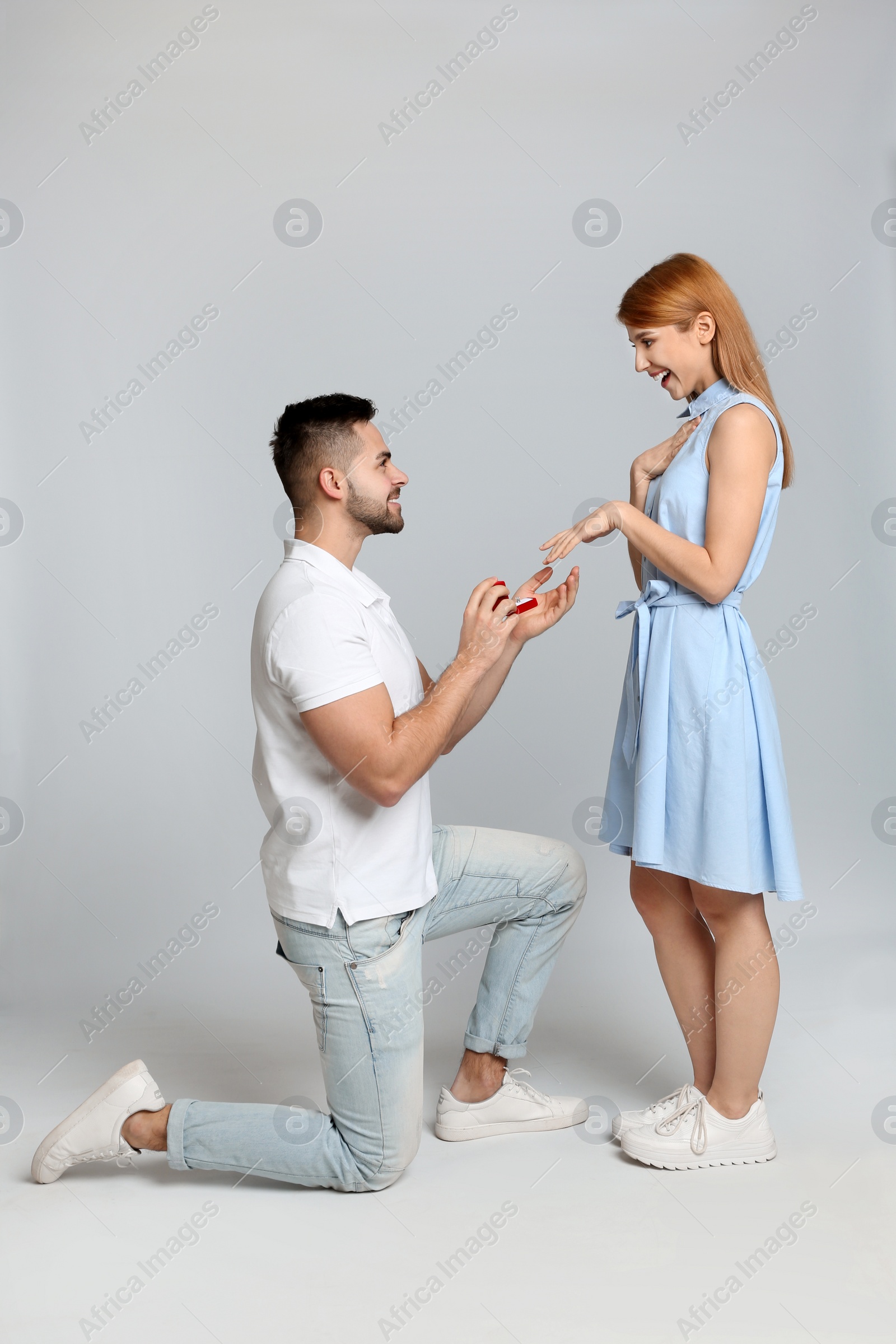 Photo of Man with engagement ring making marriage proposal to girlfriend on light grey background