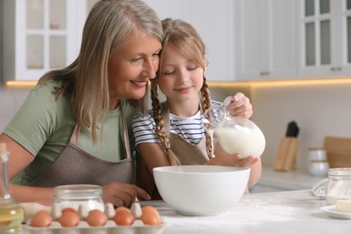 Happy grandmother with her granddaughter cooking together in kitchen