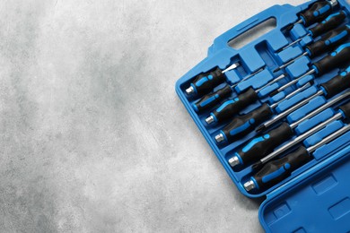 Photo of Set of screwdrivers in open toolbox on light grey textured table, top view. Space for text