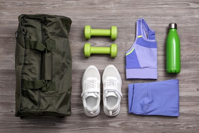 Photo of Gym bag and sports equipment on wooden background, flat lay