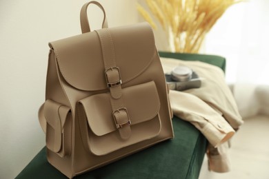 Stylish beige backpack and jacket on green bench indoors