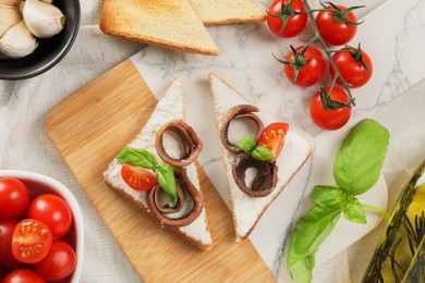 Photo of Delicious sandwiches with cream cheese, anchovies and tomatoes on light grey table, flat lay