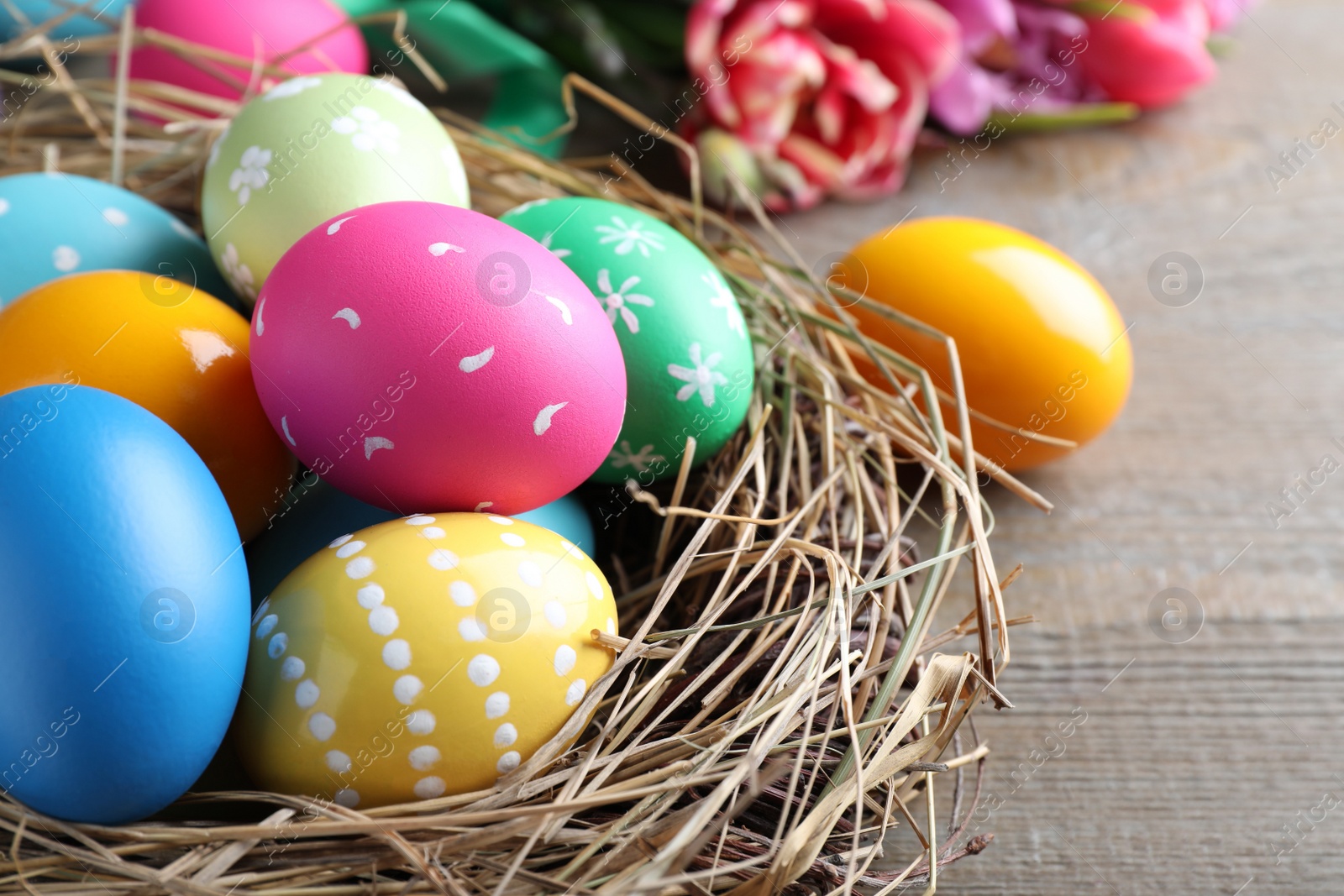 Photo of Bright painted eggs and spring tulips on wooden table, closeup. Happy Easter