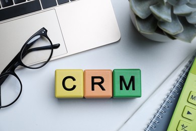 Photo of Abbreviation CRM of cubes with laptop on light office table, flat lay. Customer Relationship Management
