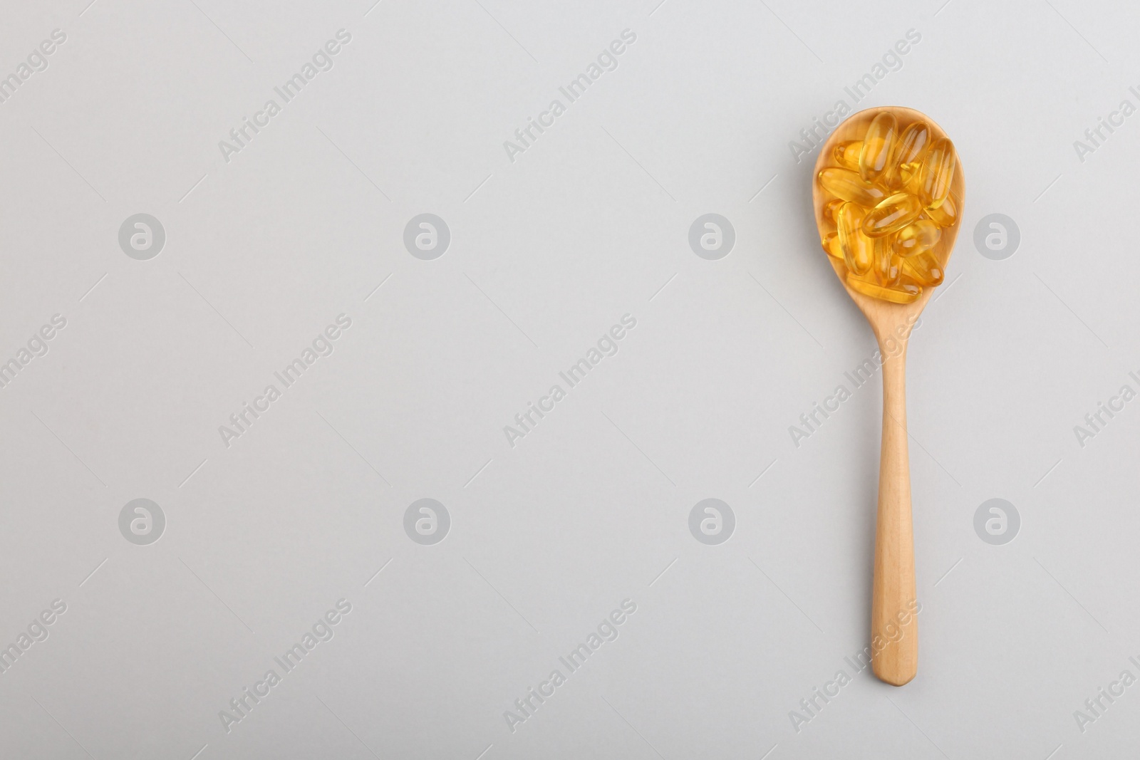 Photo of Vitamin capsules in wooden spoon on light background, top view. Space for text