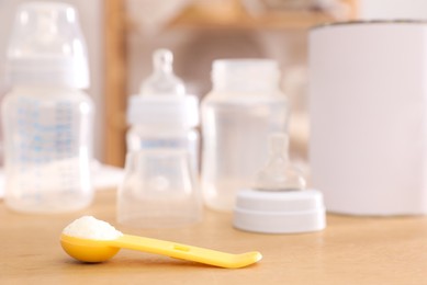 Scoop with powdered infant formula, can and bottles on wooden table indoors, space for text. Baby milk