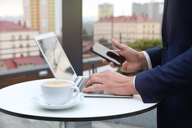 Photo of Businessman with laptop and mobile phone in outdoor cafe, closeup. Corporate blog