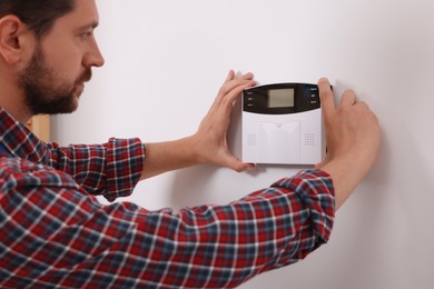 Man installing home security alarm system on white wall indoors